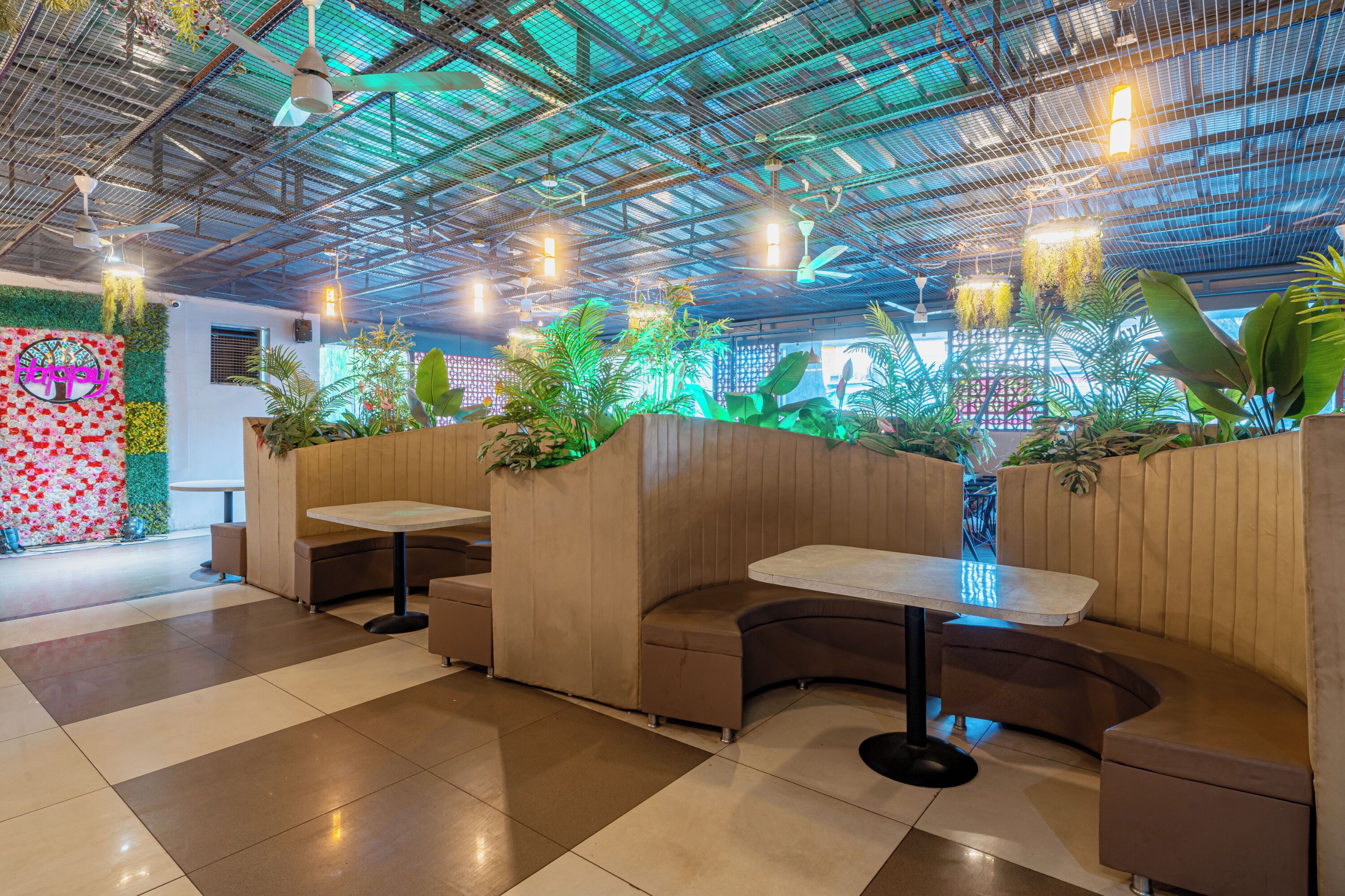 Un restaurant avec des banquettes, un plafond haut avec des poutres apparentes et des plantes vertes.