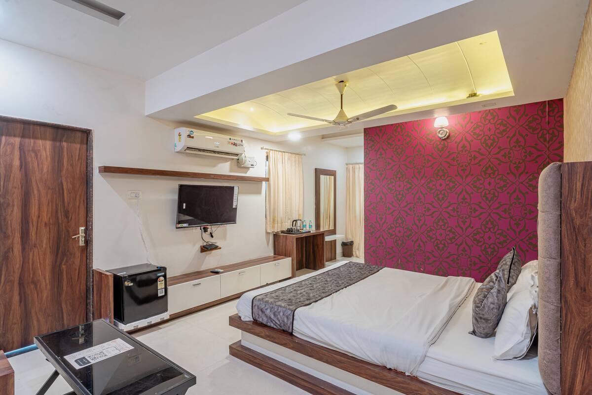 A bedroom with a bed, a TV, a desk, and a ceiling fan.