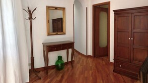 Ein Zimmer mit Holzboden, Kleiderhaken, Spiegel, einem kleinen Tisch mit einer grünen Vase und einem Schrank.