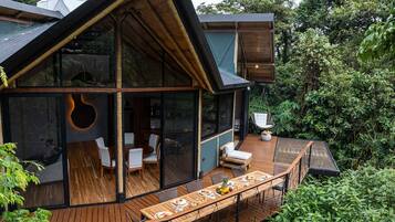 A modern house with a large glass window, wooden deck, and outdoor seating area.
