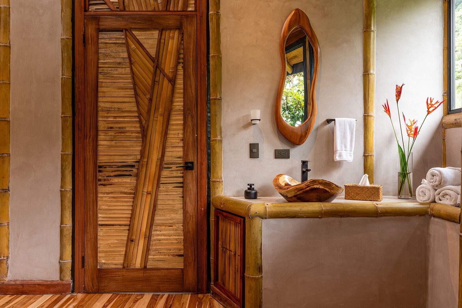 A bathroom with a wooden door, a mirror, a sink with a decorative bowl, and towels.