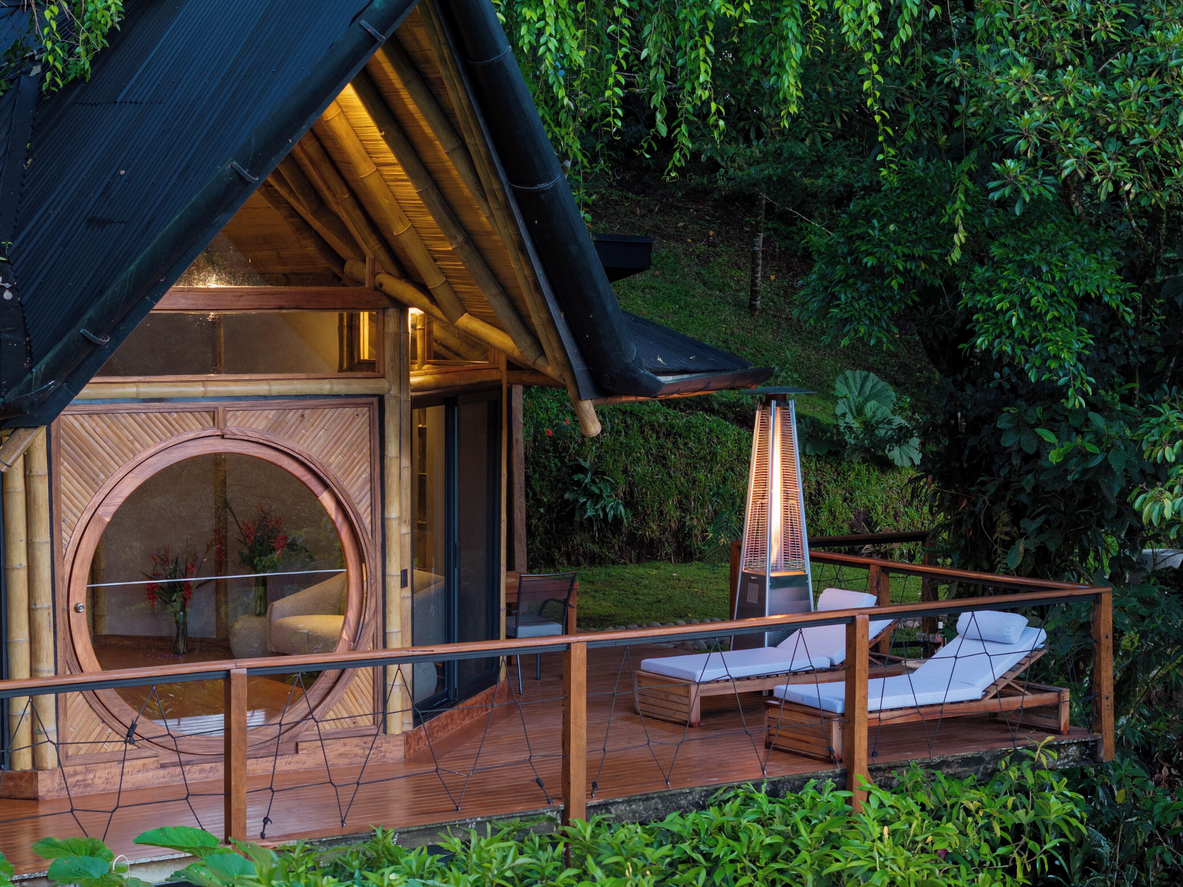 A wooden cabin with a circular glass window, a deck with lounge chairs, and a hot tub.