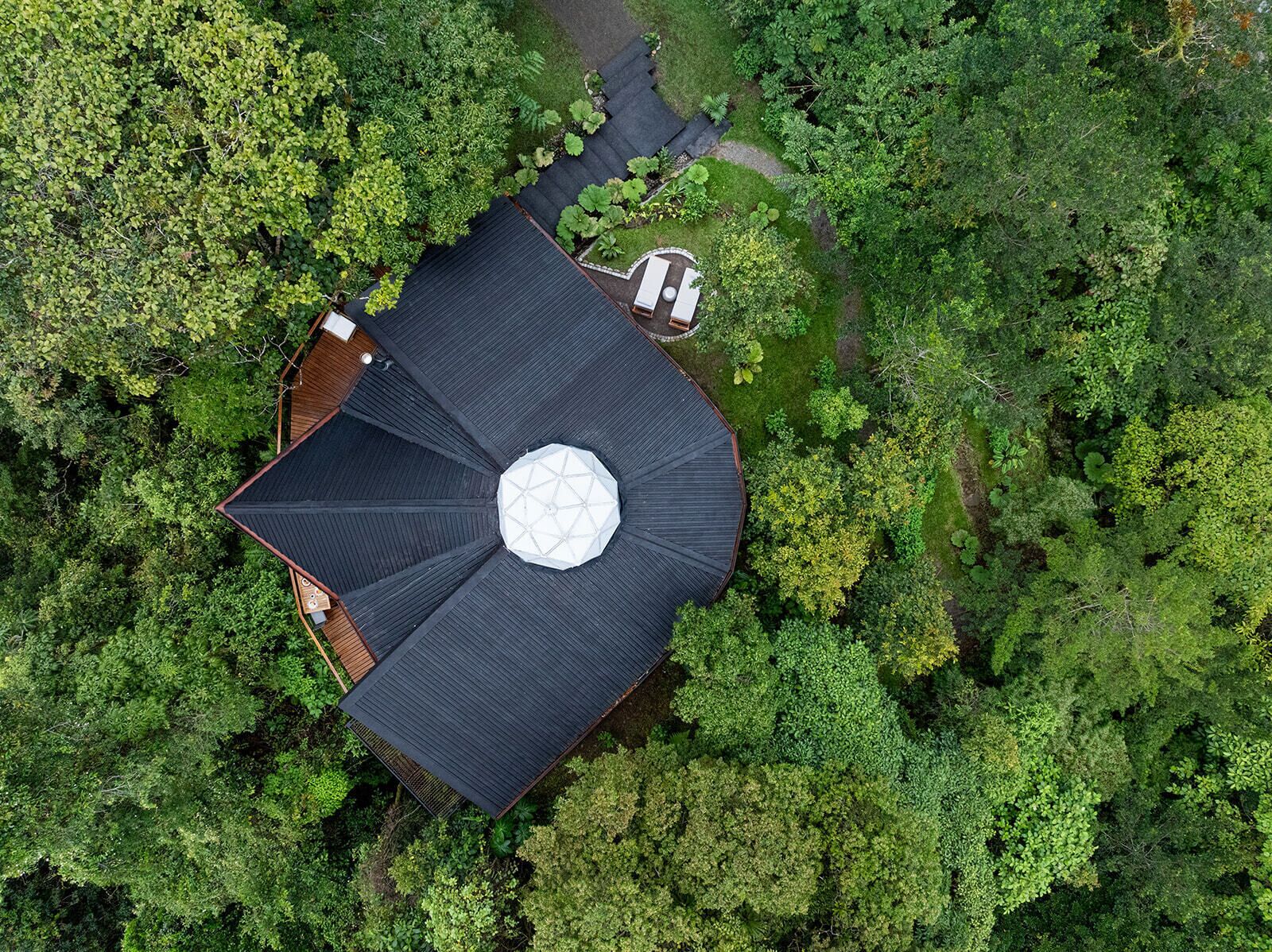 An aerial view of a circular building with a central dome, surrounded by dense greenery.