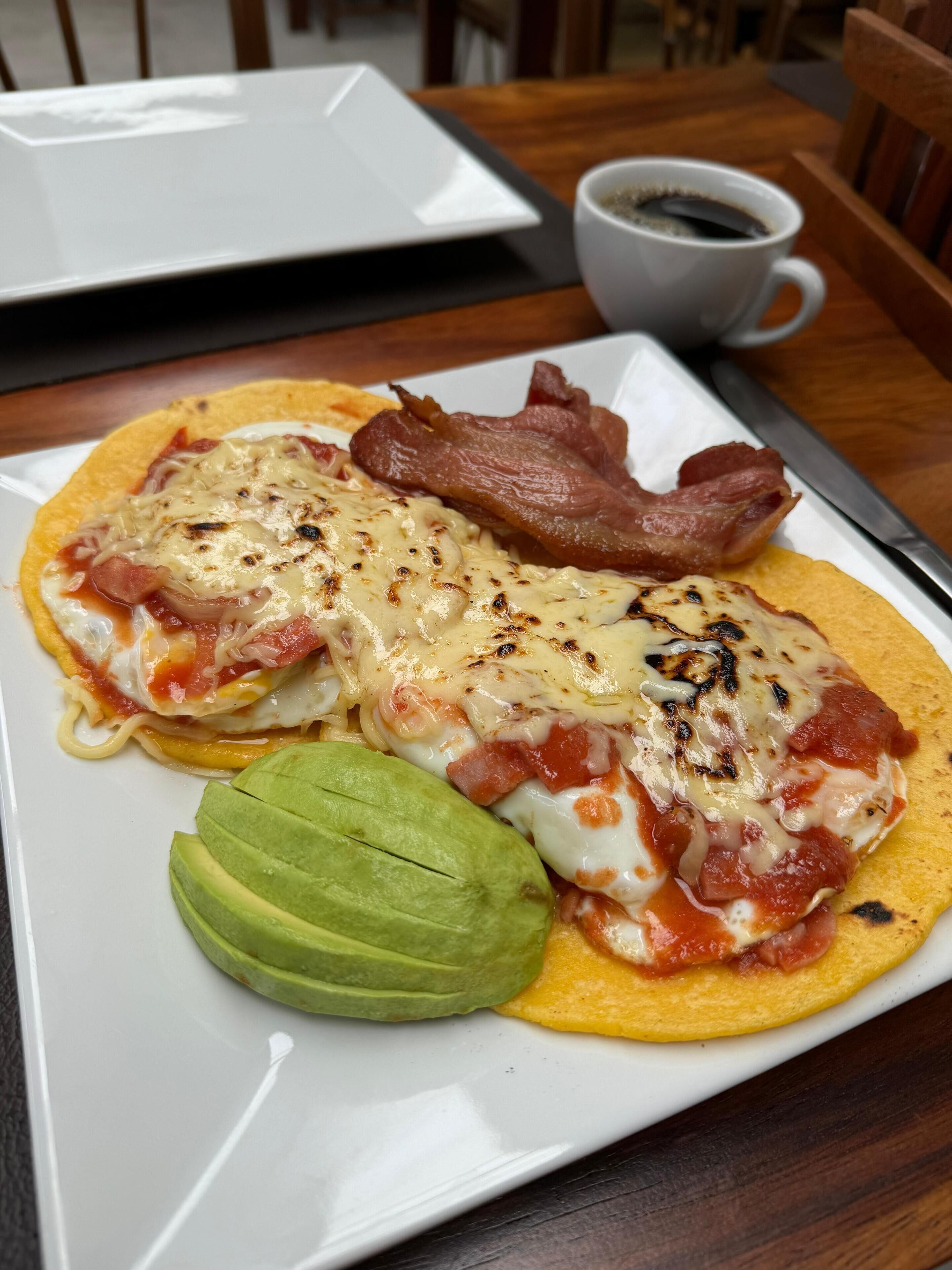 Un plato de desayuno con huevos, tocino y aguacate sobre un plato blanco.