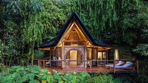 A wooden cabin with a circular glass door, a deck with lounge chairs, and a fireplace. - El Tigre Hideaway (Cabeceras)