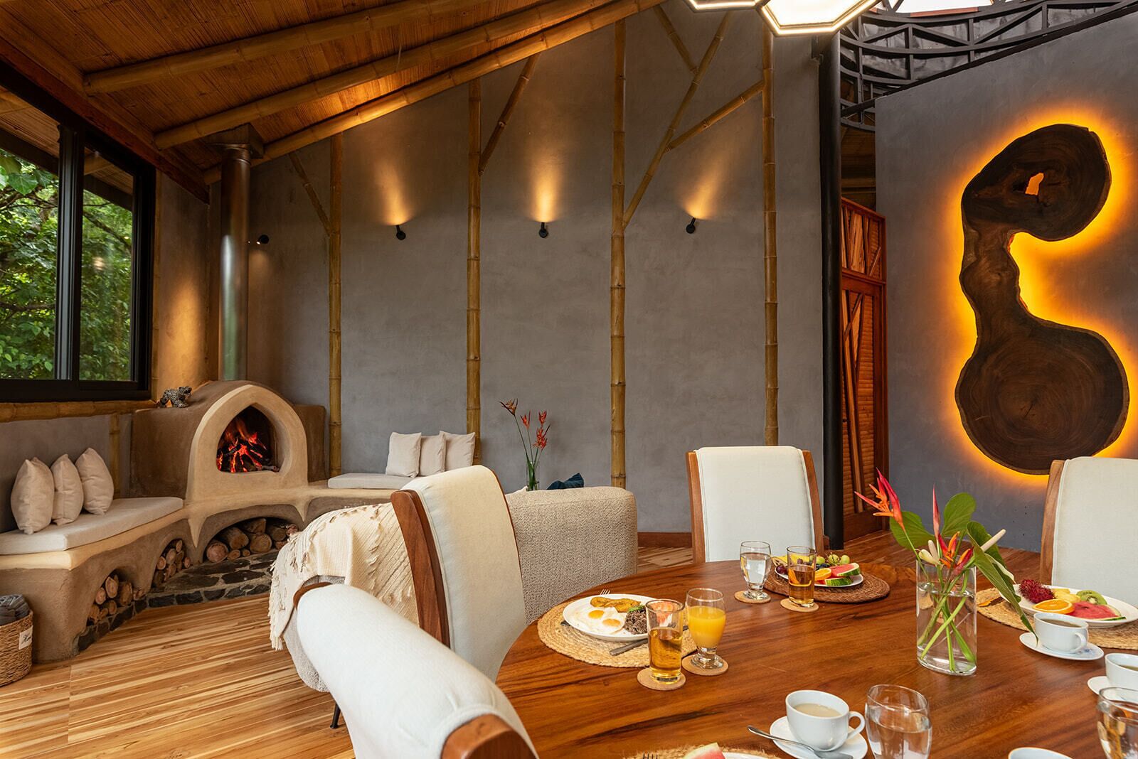 A dining area with a wooden table set for breakfast, a stone fireplace, and a large abstract wall art piece.