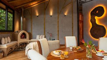 A dining area with a wooden table set for breakfast, a stone fireplace, and a large abstract wall art piece.