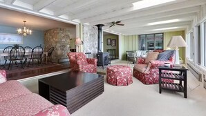 Un salon spacieux avec une cheminée, un coin repas avec des chaises, et un espace salon confortable avec des poufs et un canapé.