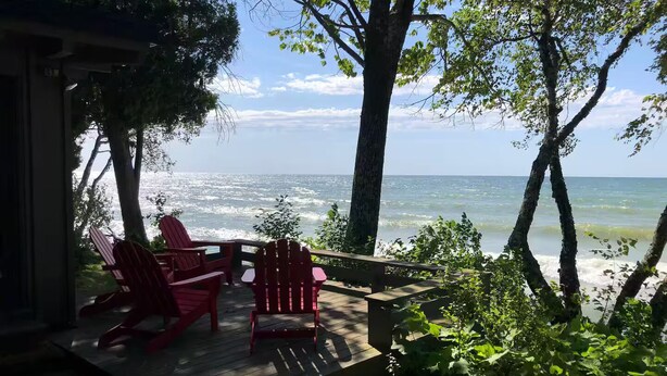 Une terrasse en bois avec des fauteuils Adirondack rouges donnant sur une étendue d’eau.