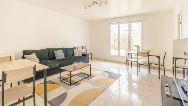 A modern living room with a green sofa, a coffee table, and a dining area with chairs and a table.