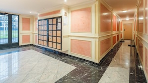 A hotel corridor with a marble floor, a large bulletin board, and a door at the end.