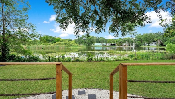 A wooden deck with a railing overlooking a lake surrounded by greenery. - Lake view + 10min to dwtn + near parks + 2 guests! (Orlando)