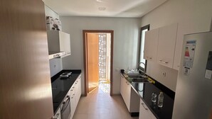 A narrow kitchen with white cabinets, a black countertop, and a refrigerator. - THE ESCAPE FROM BOUREGREG (Salé)