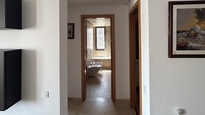 A hallway leading to a bathroom with a window, a framed picture on the wall, and a small shelf with a bottle. - THE ESCAPE FROM BOUREGREG (Salé)