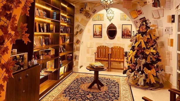 A warmly lit room with a large bookshelf, a Christmas tree, and a chandelier. - The Reds Pousada (Penha)