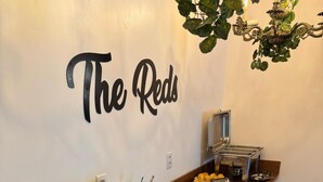 A buffet setup with various food items and drinks, a wall sign reading "The Reds", and a chandelier. - The Reds Pousada (Penha)