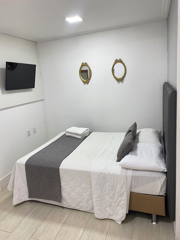 A modern bedroom with a bed, bedside tables, a flat-screen TV, and two wall-mounted mirrors. - The Reds Pousada (Penha)