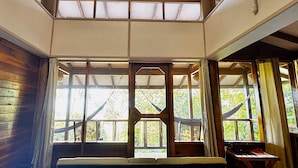A room with a sloped ceiling, wooden beams, and large windows with curtains. - Samasati Rainforest Bungalows (Cahuita)