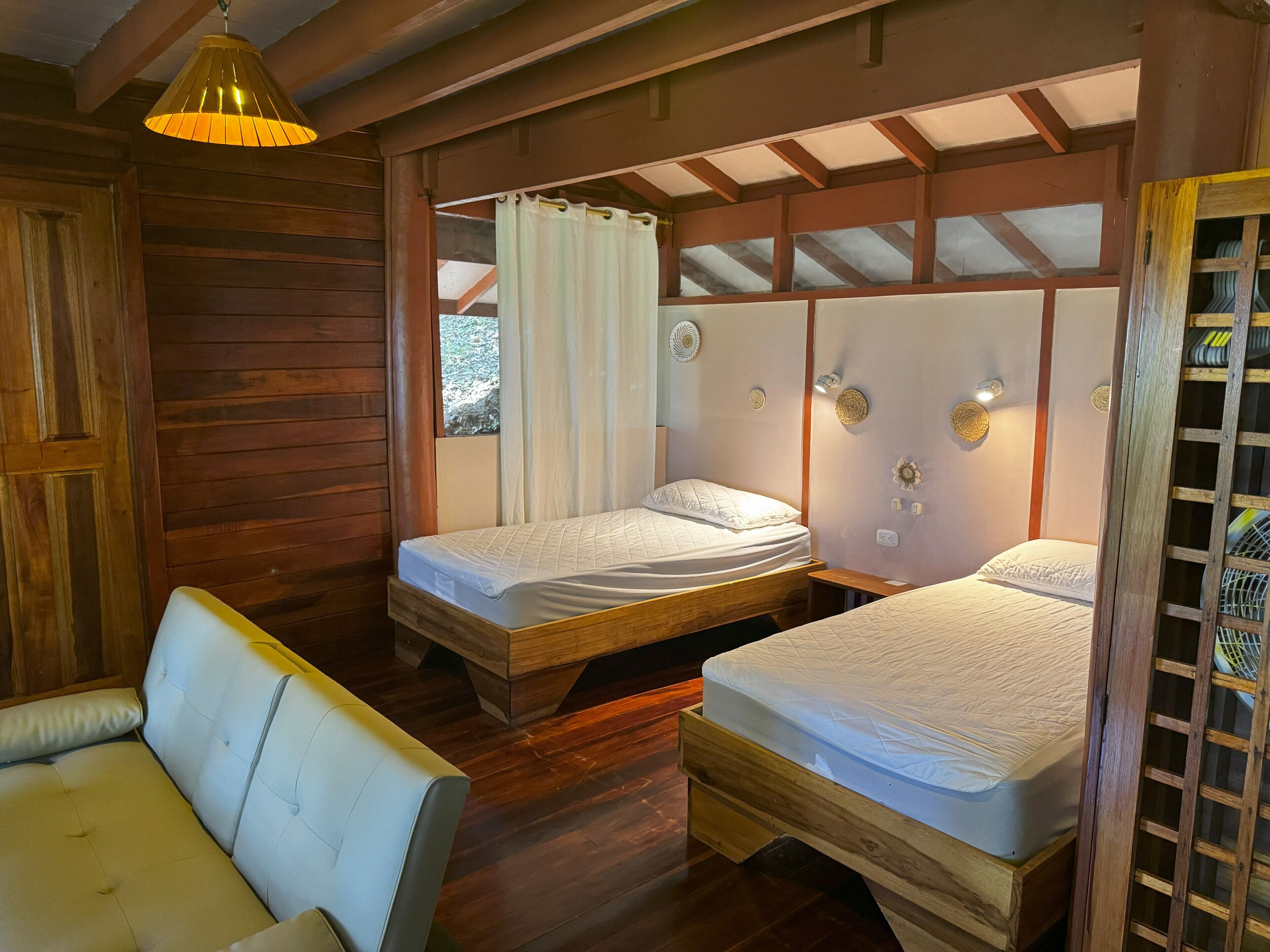 A cozy room with two wooden beds, a cushioned bench, and a hanging light fixture.