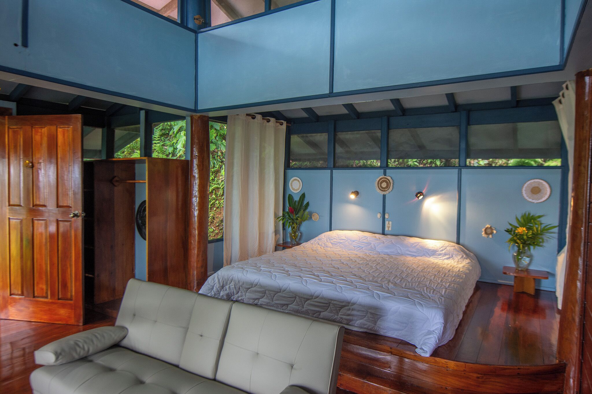 A bedroom with a bed, a sofa, and a wooden door.