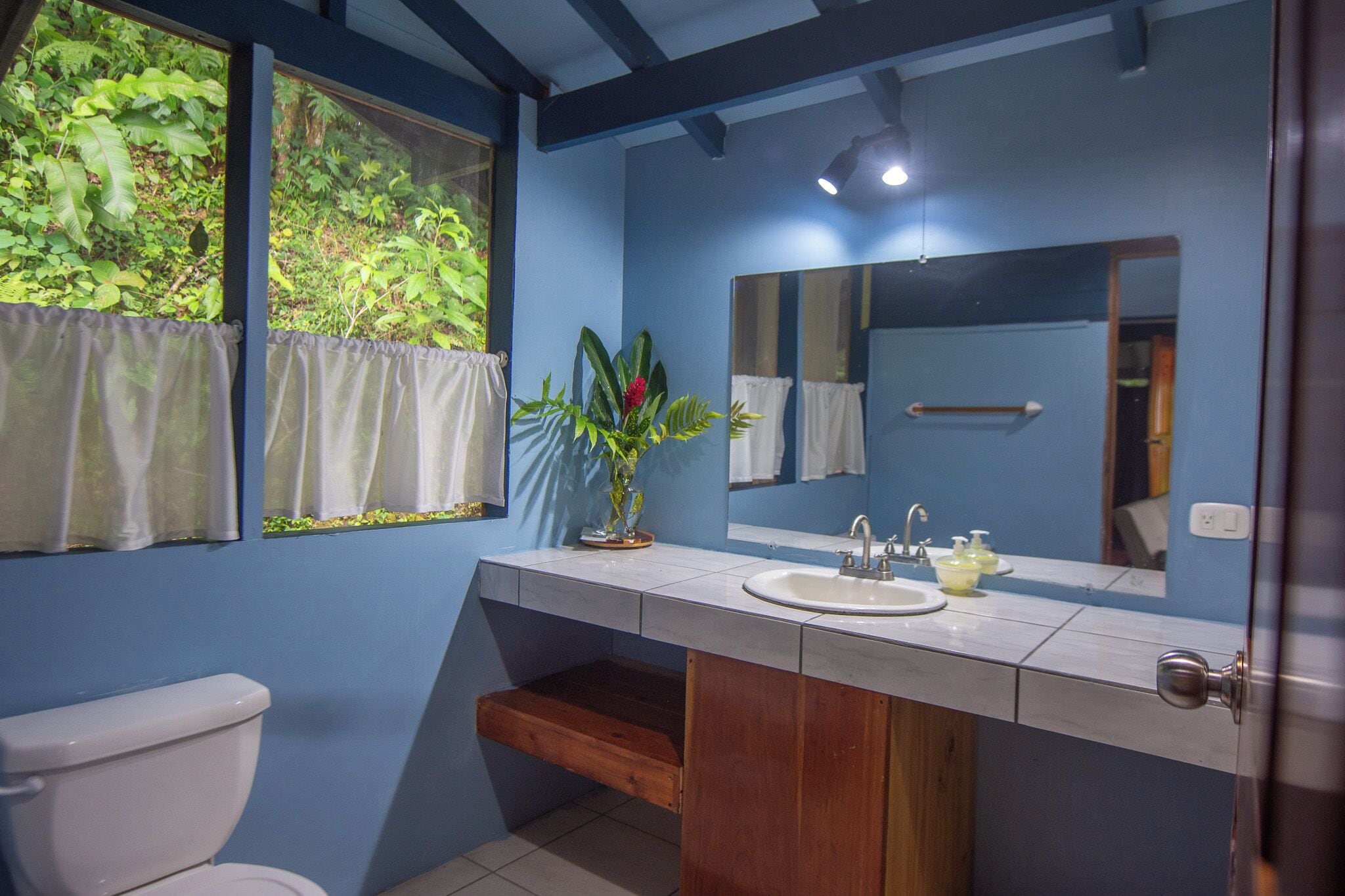 A bathroom with a blue wall, a white sink, a mirror, and a window with curtains.