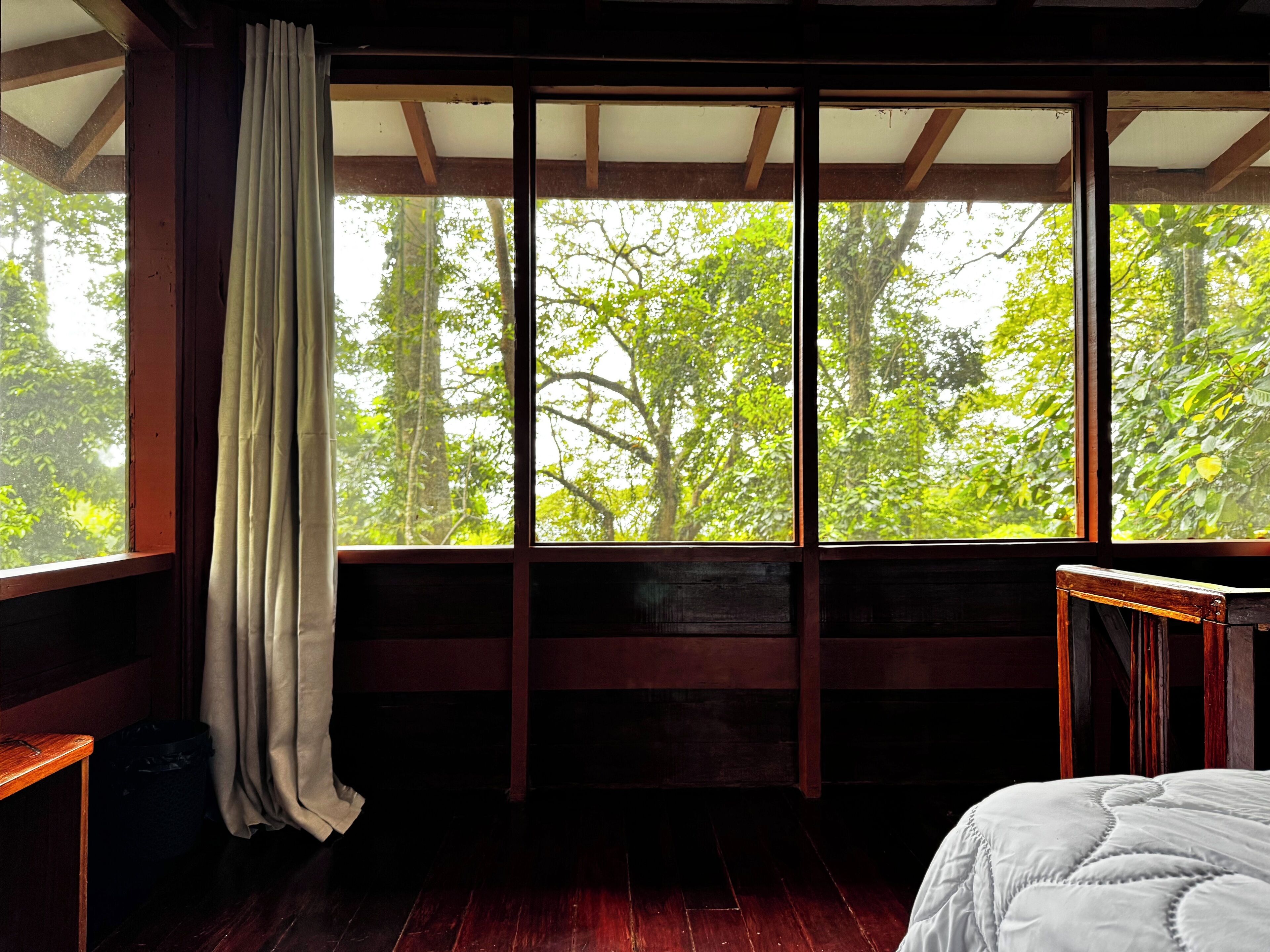 A room with a large window, wooden beams, a bed, and a small table.