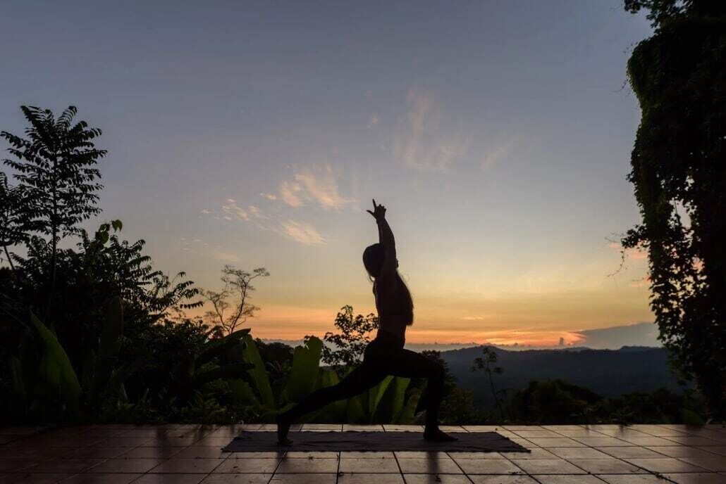 A person performing a yoga pose on a tiled platform with a scenic sunset view.