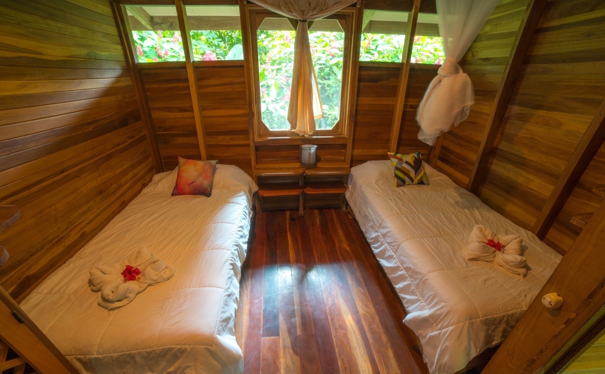 Una cabaña con dos camas de madera, una mesita y un ventanal con vistas a la vegetación.