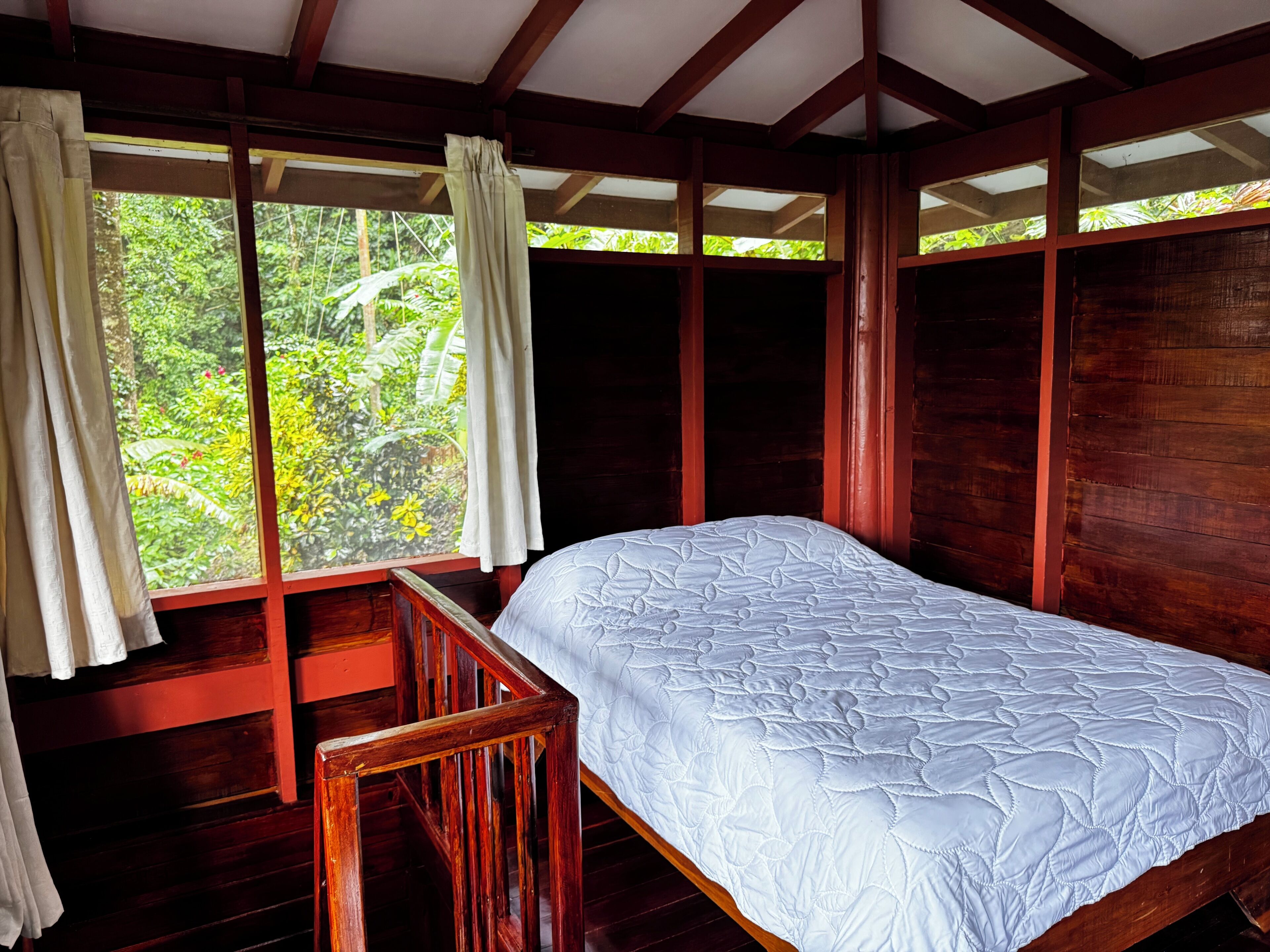 A wooden room with a bed, large windows, and curtains.