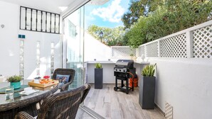 An outdoor patio with a dining table, wicker chairs, a grill, potted plants, and a white fence. - Los Naranjos / Puerto Banus apartment (Nueva andalucia)