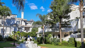 A courtyard with a central white structure, surrounded by lush greenery and white buildings with balconies. - Los Naranjos / Puerto Banus apartment (Nueva andalucia)