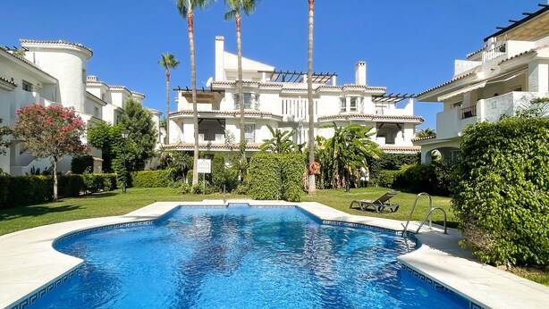 A swimming pool surrounded by lush greenery and white buildings with balconies. - Los Naranjos / Puerto Banus apartment (Nueva andalucia)