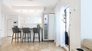 A modern kitchen with a central island, bar stools, pendant lights, and a view of the living area through a glass door. - Los Naranjos / Puerto Banus apartment (Nueva andalucia)