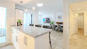 A modern kitchen with a central island, pendant lighting, and a dining area with chairs and a table. - Los Naranjos / Puerto Banus apartment (Nueva andalucia)