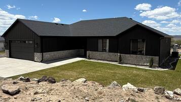 A modern two-story building with a garage, a covered patio, and a landscaped lawn.