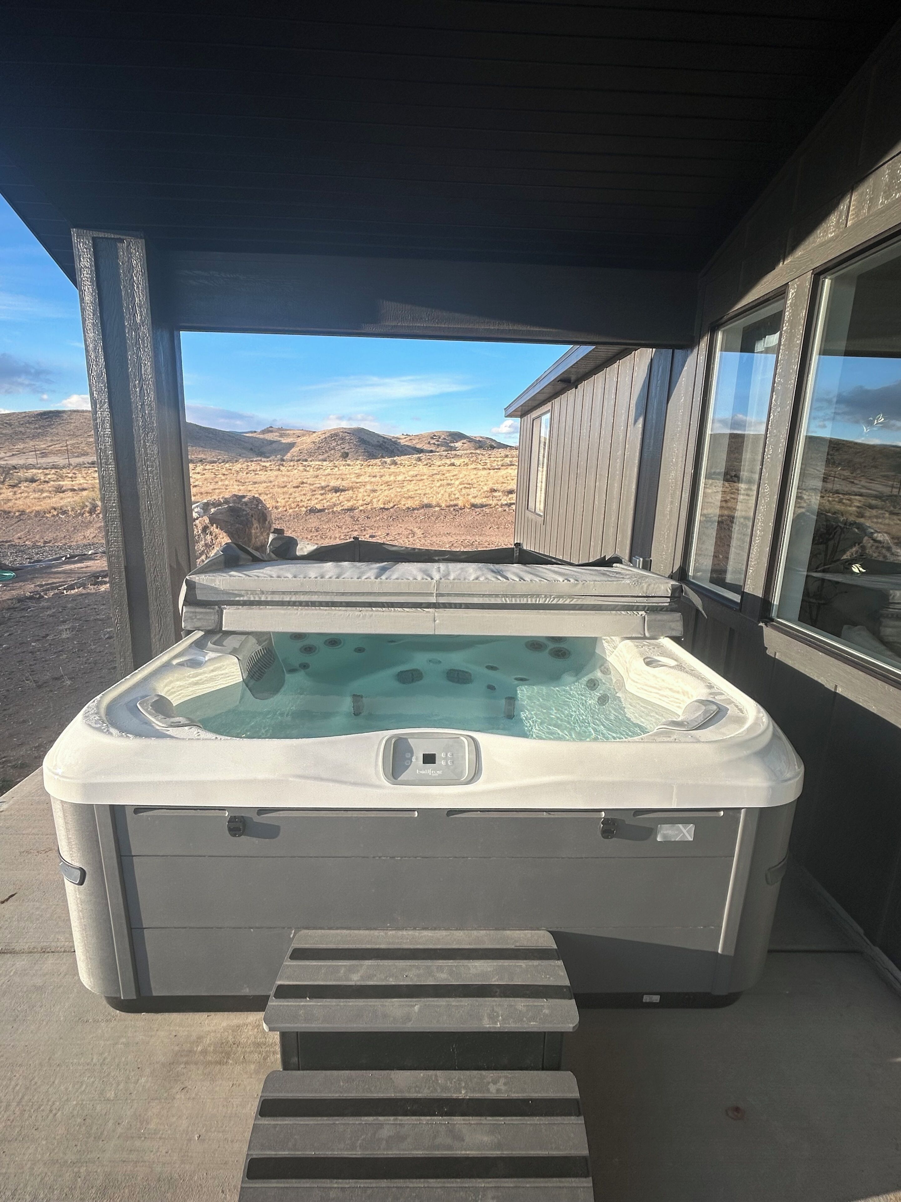 A hot tub with a control panel, steps leading up to it, and a view of a desert landscape through a window.
