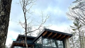 Een modern huis met grote glasramen, een houten terras en een gevel van natuursteen.