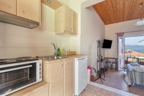 A compact kitchen with a built-in oven, a small refrigerator, and a dining area with a table and chairs. - Studio Apartment 'Two Adults No 2' with Sea View, Wi-Fi and Air Conditioning (Nikiana)