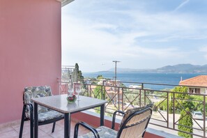 Un balcón con mesa y sillas, con vista al mar y montañas a lo lejos.