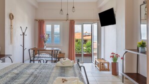 A hotel room with a bed, a desk, a chair, a TV, a balcony with a view, and a window. - Studio Apartment '3 Adults No 4' with Sea View, Wi-Fi and Air Conditioning (Nikiana)