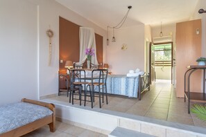 Una habitación con una cama, una mesa de comedor con sillas, una mesita con un florero y vistas al exterior.