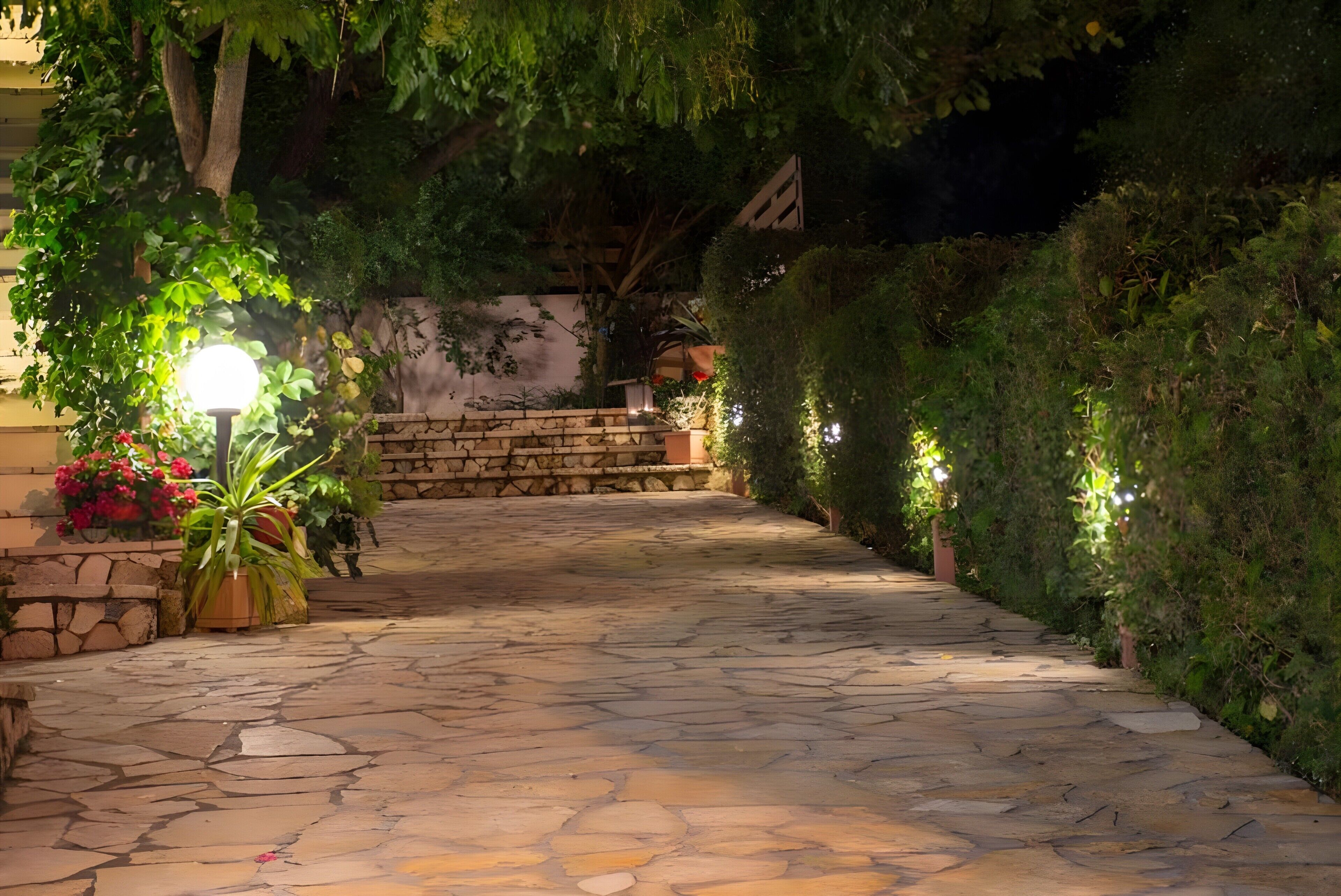 A stone pathway leading to a building, surrounded by lush greenery and stone walls.