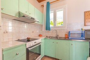 Una cocina con armarios azul turquesa, estufa, horno, lavabo y una ventana con cortina.