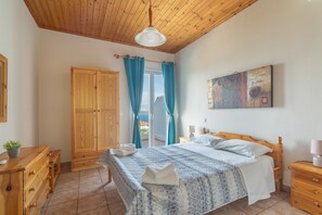 Un dormitorio con techo de madera, una cama con colcha azul y blanca estampada, un armario de madera, una mesita de noche de madera y un cuadro en la pared.