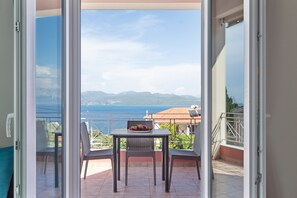 Balcón abierto con mesa y sillas, vista al mar y a las montañas, y barandilla.
