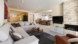 Una sala moderna con un sofá seccional, un comedor, una cocina y una chimenea de piedra.