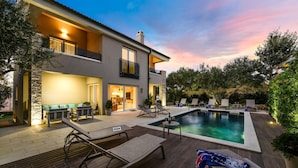 Una casa moderna con piscina, mobiliario exterior y un patio bien iluminado.