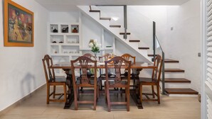 Un comedor con una mesa y sillas de madera, una escalera y una pared blanca con estantes.