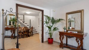 Una habitación con zona de comedor, planta en maceta, espejo y consola.