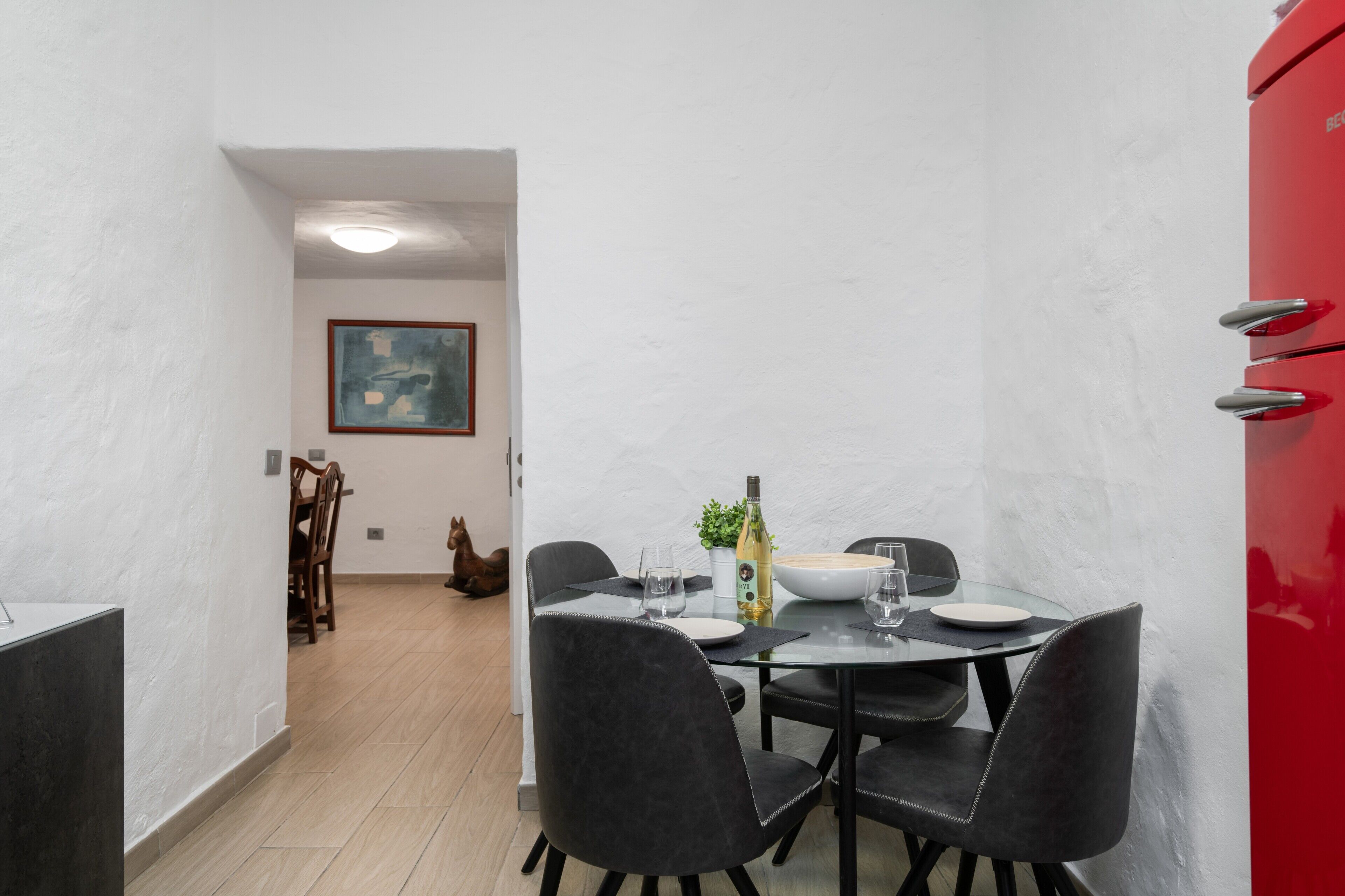 A dining area with a round table, black chairs, a red cabinet, and a framed picture on the wall.